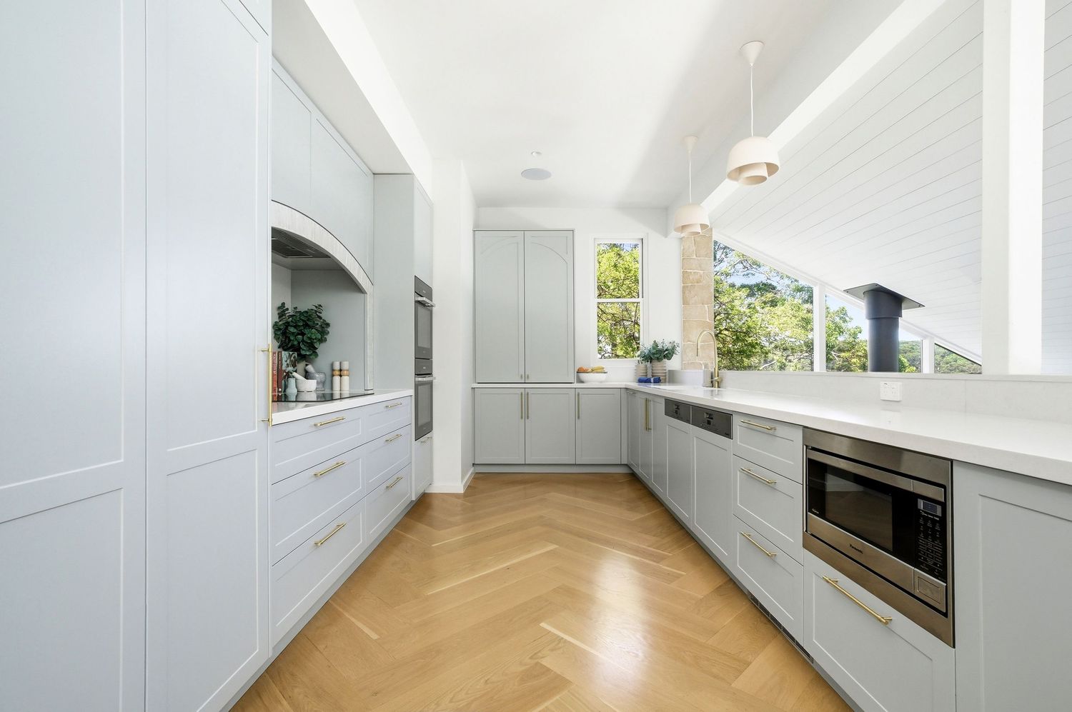 Elegant galley kitchen with light gray cabinetry, herringbone hardwood floors, white countertops, and stainless steel appliances.