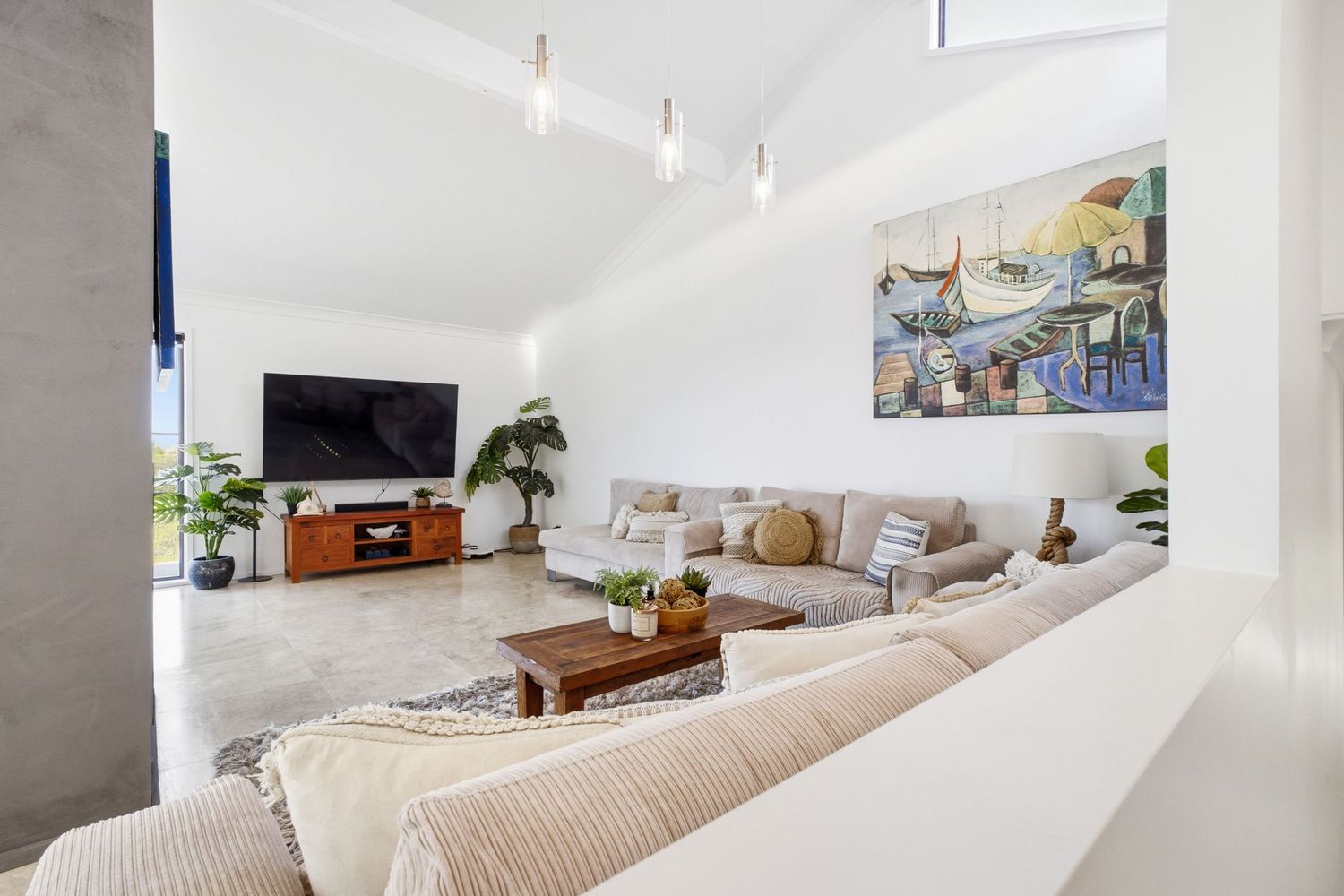 Bright modern living room with high ceilings, large sectional sofa, wall-mounted TV, and colorful artwork in a coastal home.