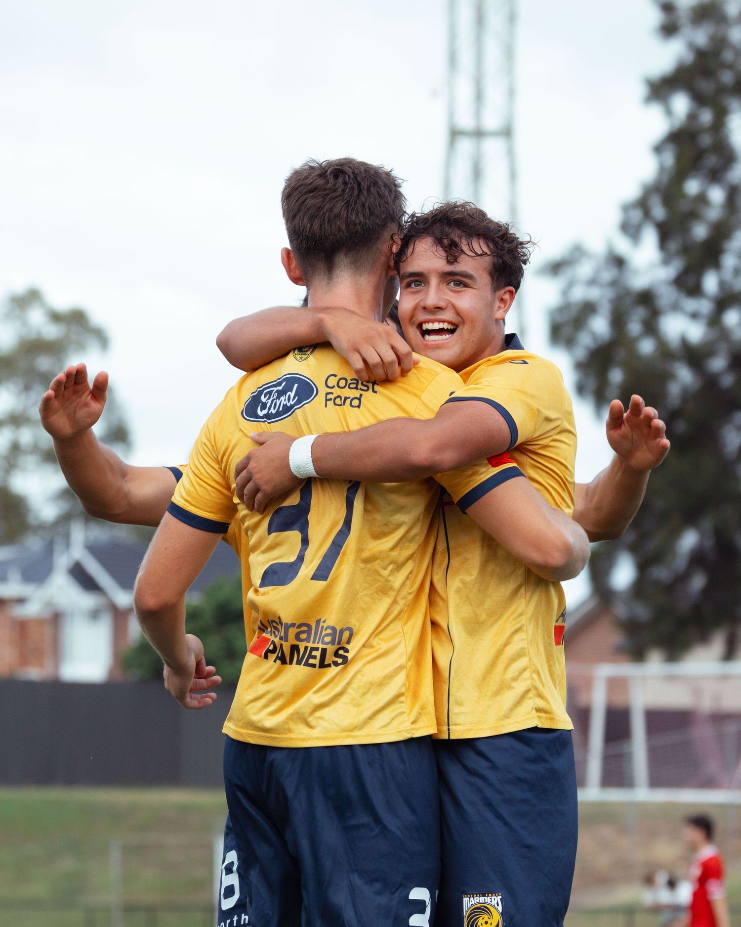 Sutherland shire sports photographer captures Two teammates in yellow jerseys celebrating with an emotional embrace on the soccer field.
