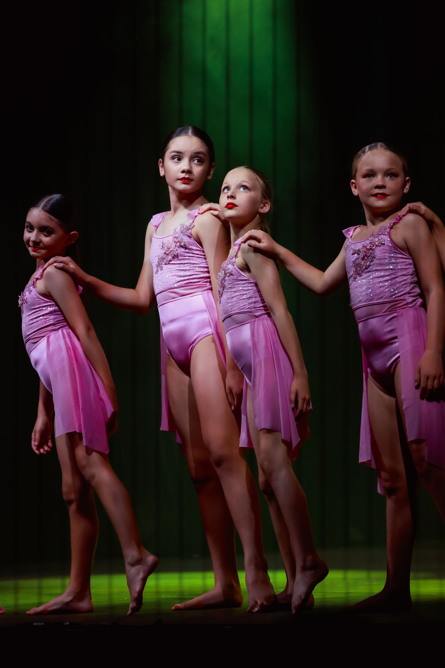 Wollongong dance photographer Young dancers in pink costumes perform a synchronized dance routine on a dark stage with green lighting.