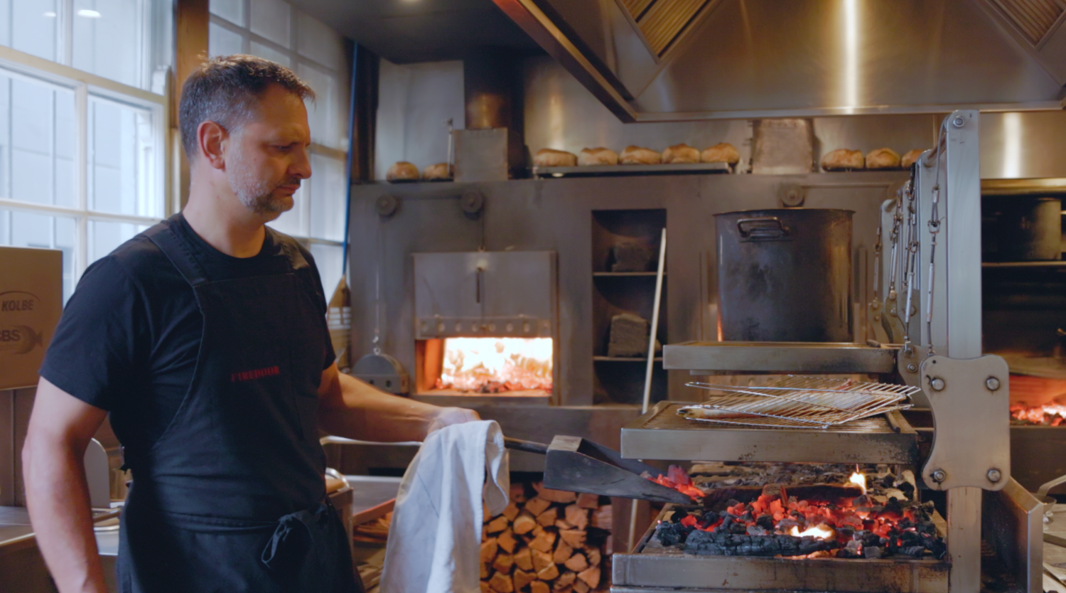 Wollonogong based videographer captures Lennox Hastie Restaurant kitchen with wood-burning grill and flames visible during food preparation.