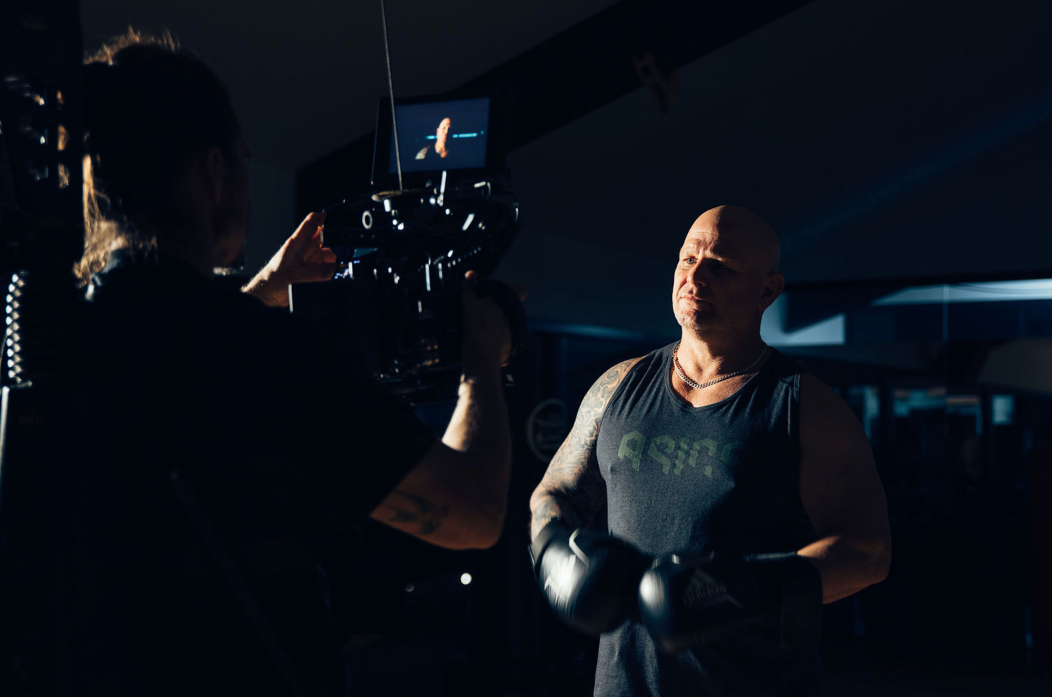 Professional videographer in sydney operating a camera rig in a dark studio setting with dramatic lighting of an athelete