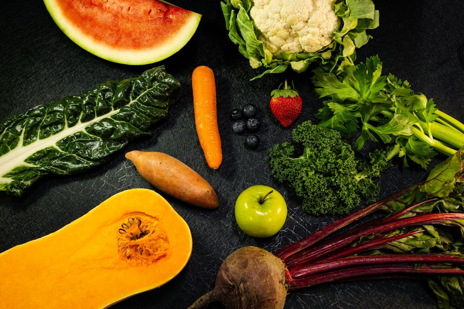 Food and product photography and videographFresh colorful vegetables and fruits arranged on dark background including watermelon and squash.