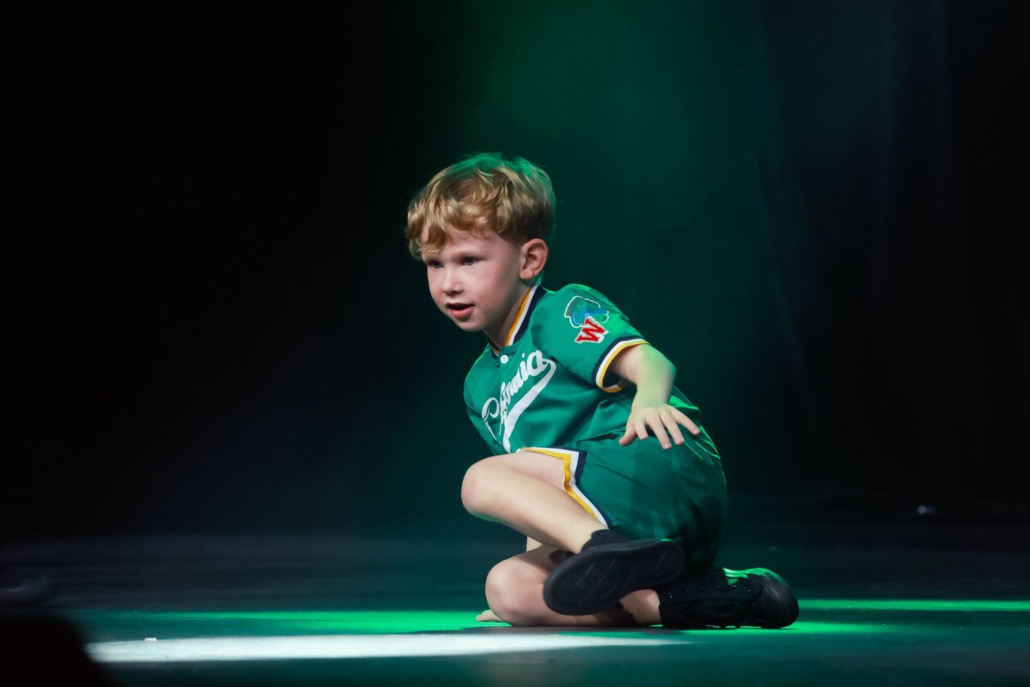 Sydney concert photographer and videographer captures Young performer in green costume rolls across stage floor under emerald lighting.