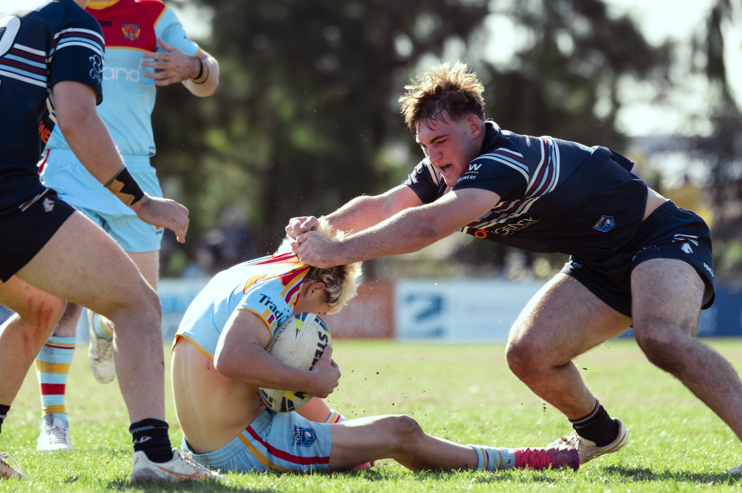 Sydney sports photographer captures players making a tackle during competitive match on grass field.