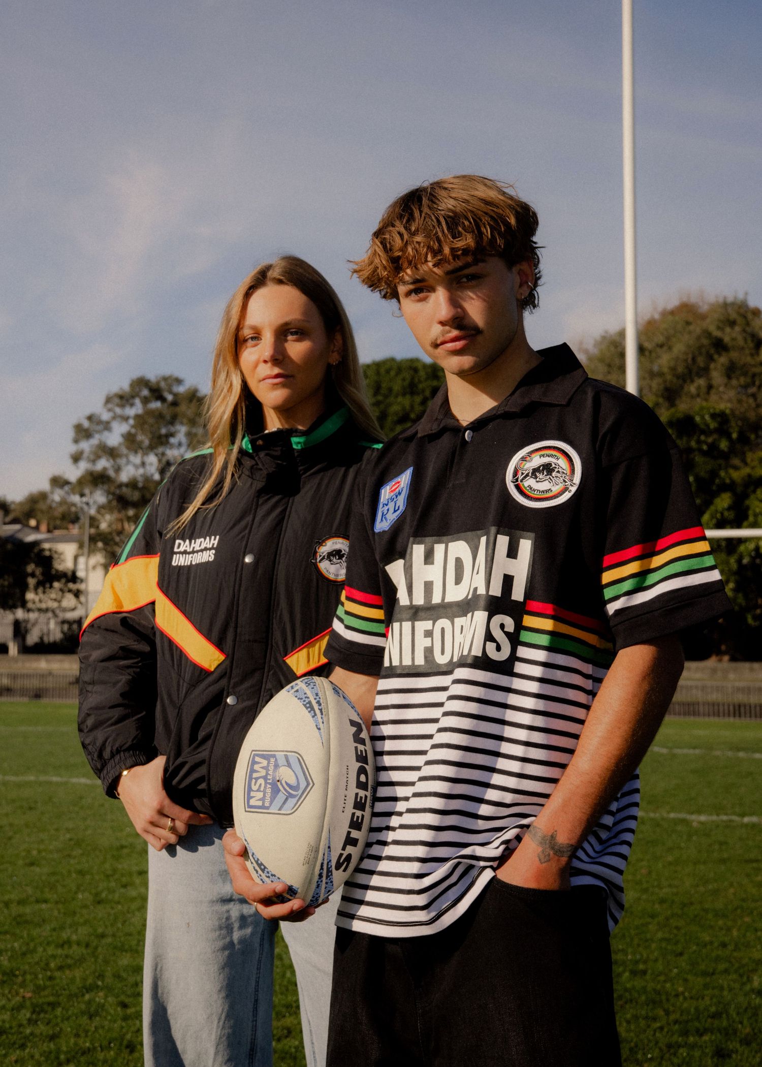 Two young people wearing Penrith Panthers NRL jerseys and jacket on a rugby field, holding a football. Sutherland Shire videographer