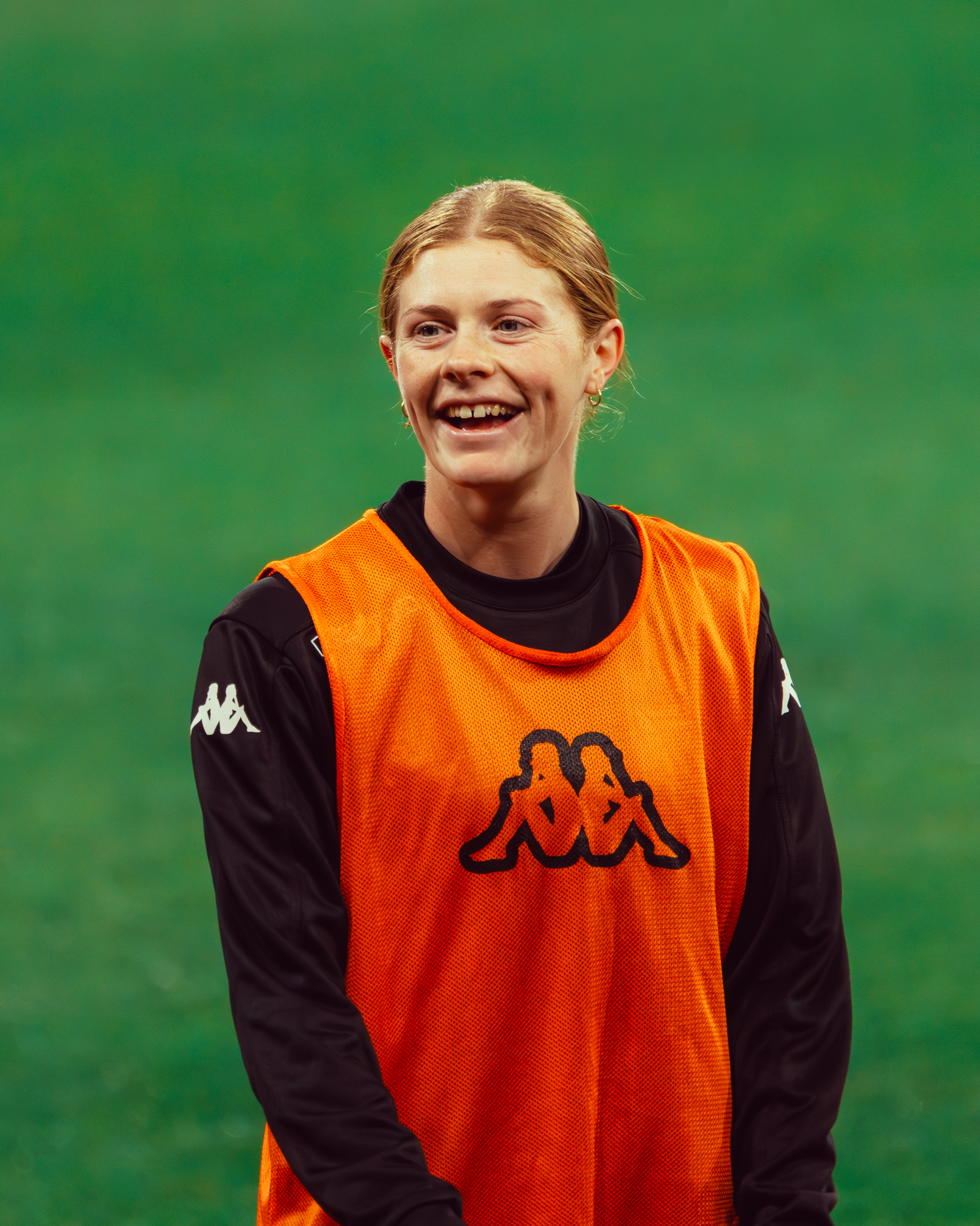 Cortnee Vine matildas player sports photographer captures Soccer player wearing orange training bib smiling during practice session.