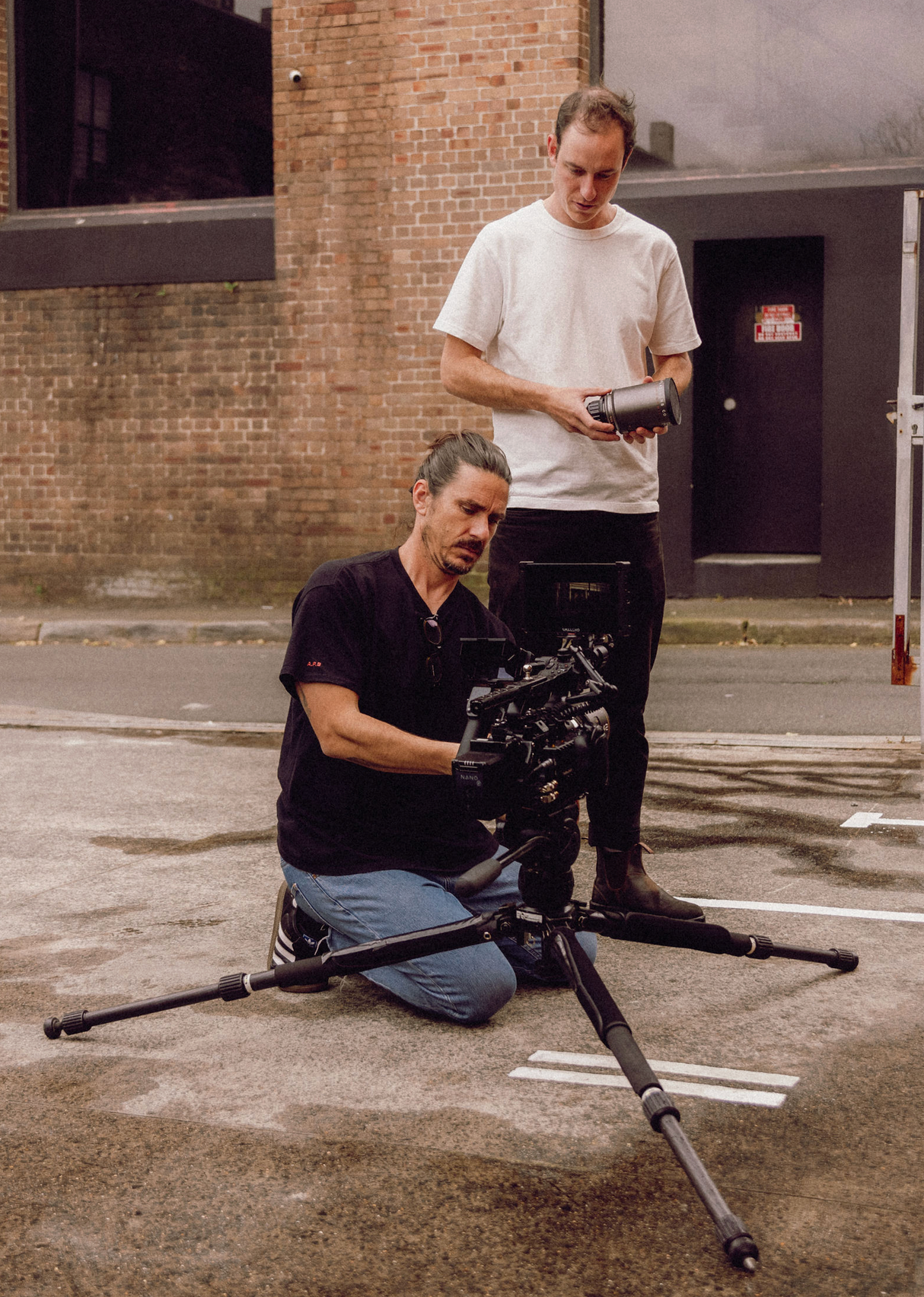 Camera operator setting up equipment on concrete floor against brick wall background. Professional videographer in sydney