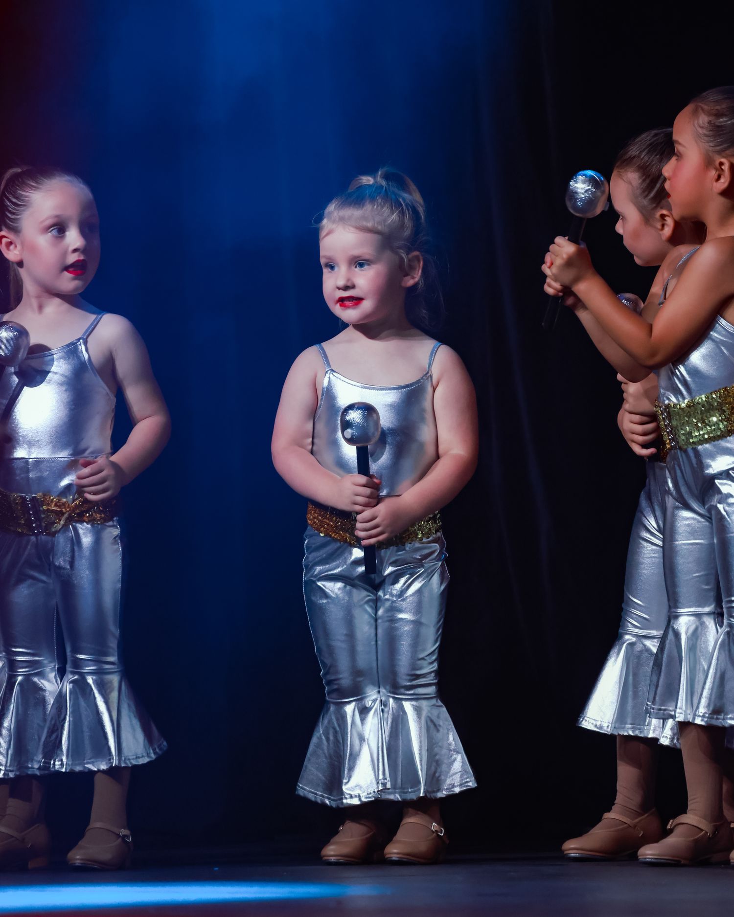 Wollongong dance and concert photographer Young dancers in silver metallic dresses perform on stage under blue lighting.