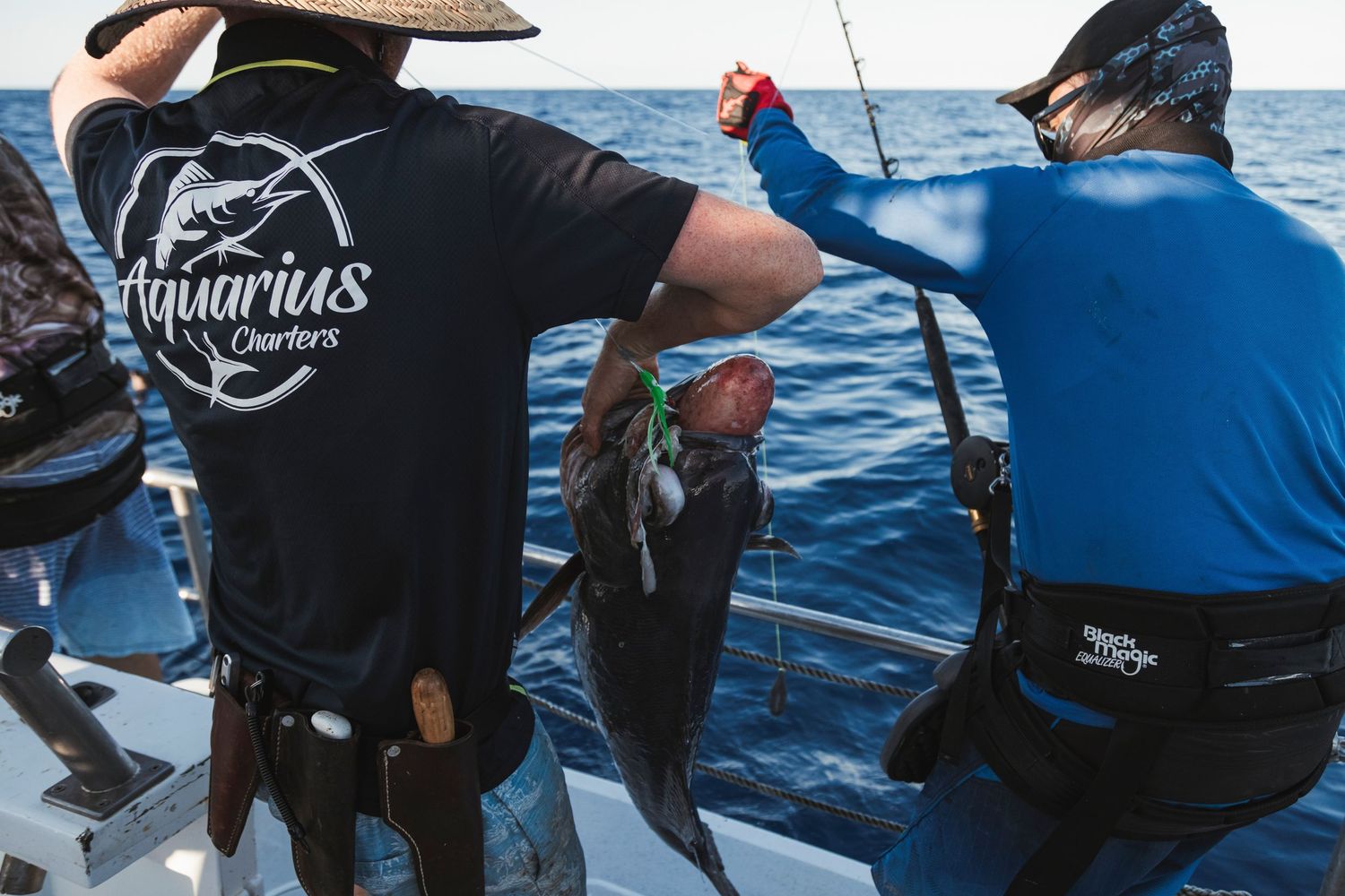 Aquarius Charters crew members holding a large caught fish on a deep sea fishing boat.