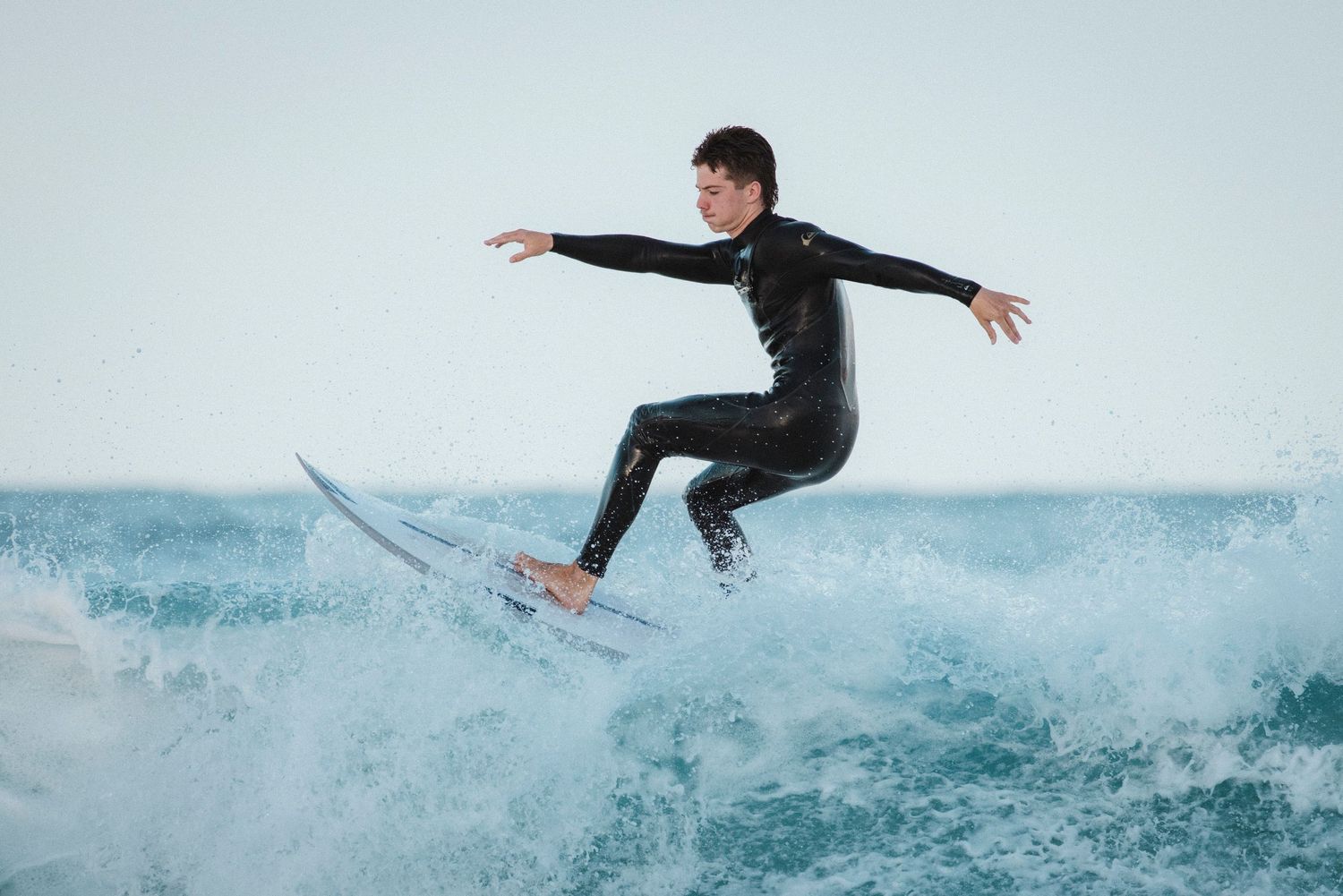 Sutherland Shire photographer Surfer in black wetsuit performs aerial maneuver on ocean wave against light blue sky in cronulla