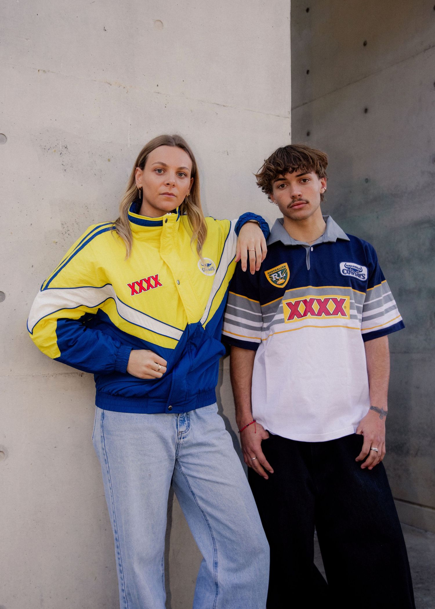 Two models wearing retro XXXX-branded yellow and blue NRL rugby league jackets and jerseys against a concrete wall. Sutherland Shire photo