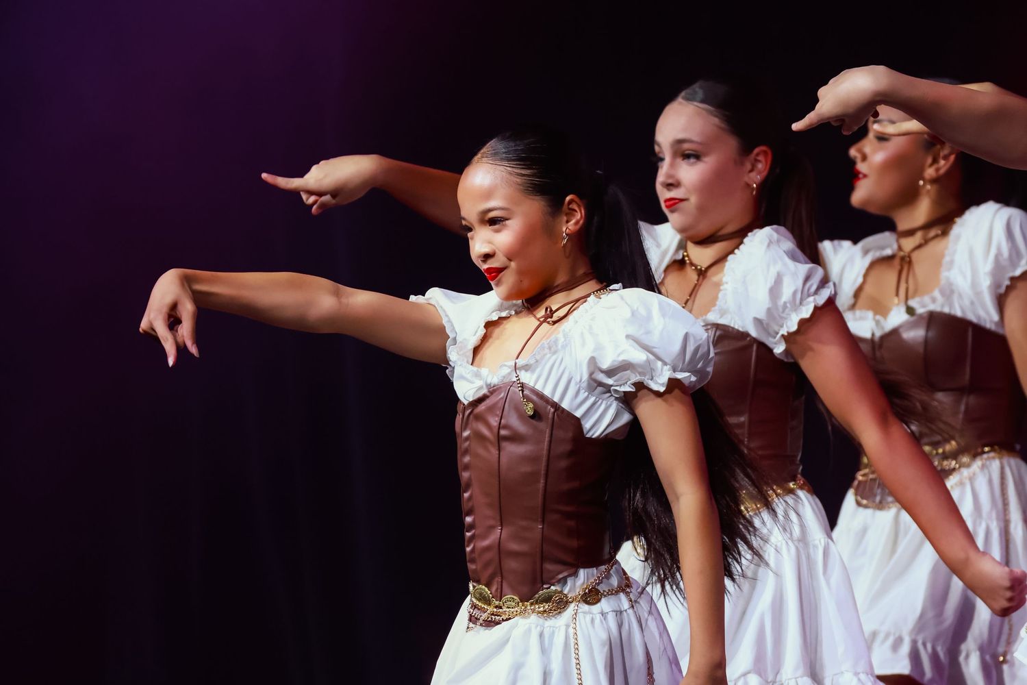Sydney concert photographer Dance troupe in white dresses and brown corsets performs coordinated arm movements on stage.