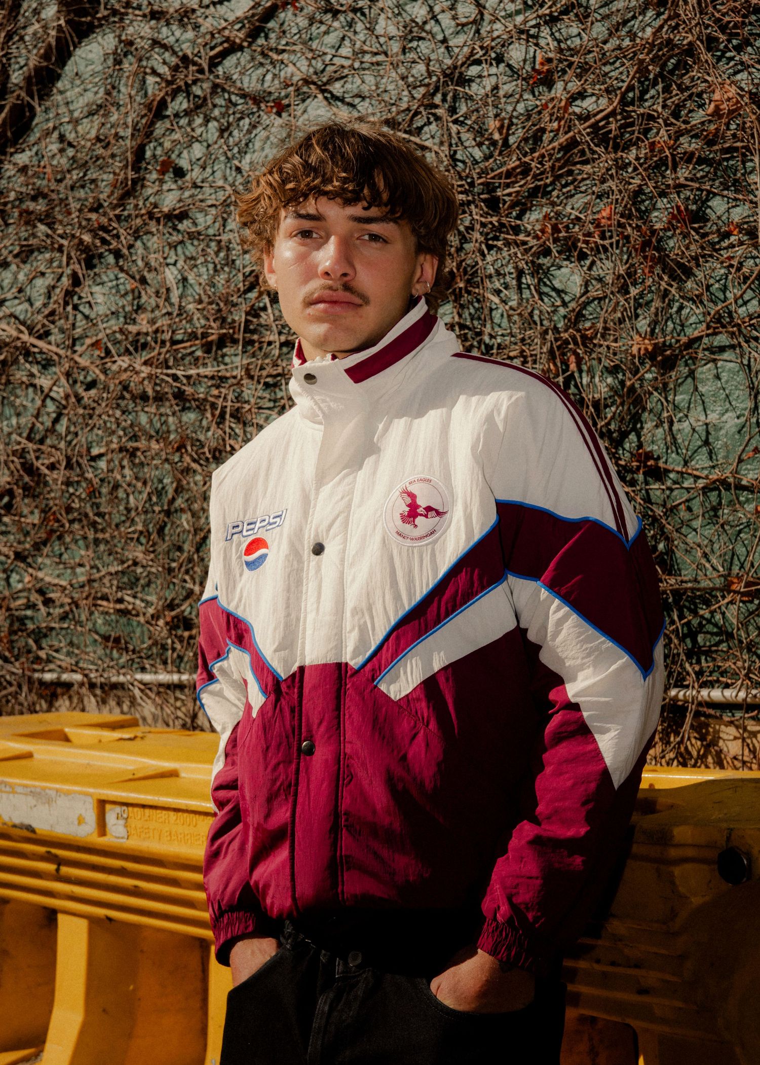 Sydney Photographer - Young man in vintage Pepsi windbreaker jacket posing outdoors against dried vines background.