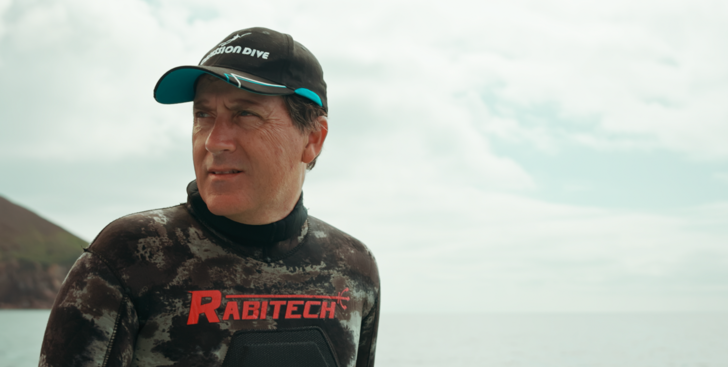 Sydney Sutherland Underwater professional photography and videography Person in diving gear wearing a cap against coastal background Sydney