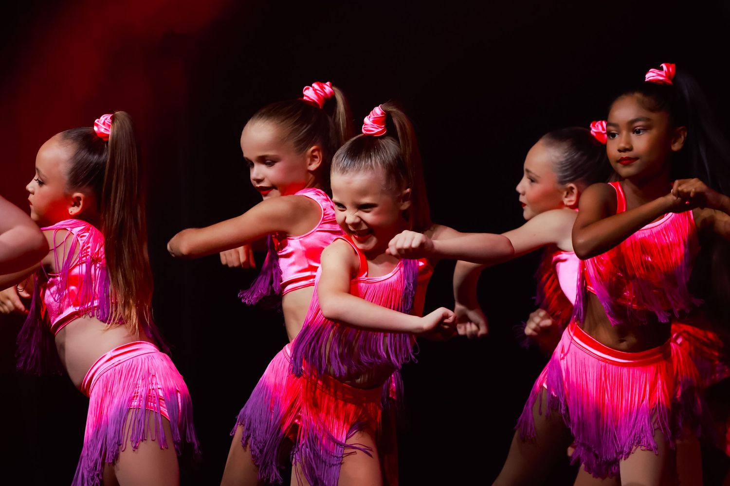 Wollongong concert photographer Young dancers in pink costumes perform on stage under dramatic lighting during a dance recital.