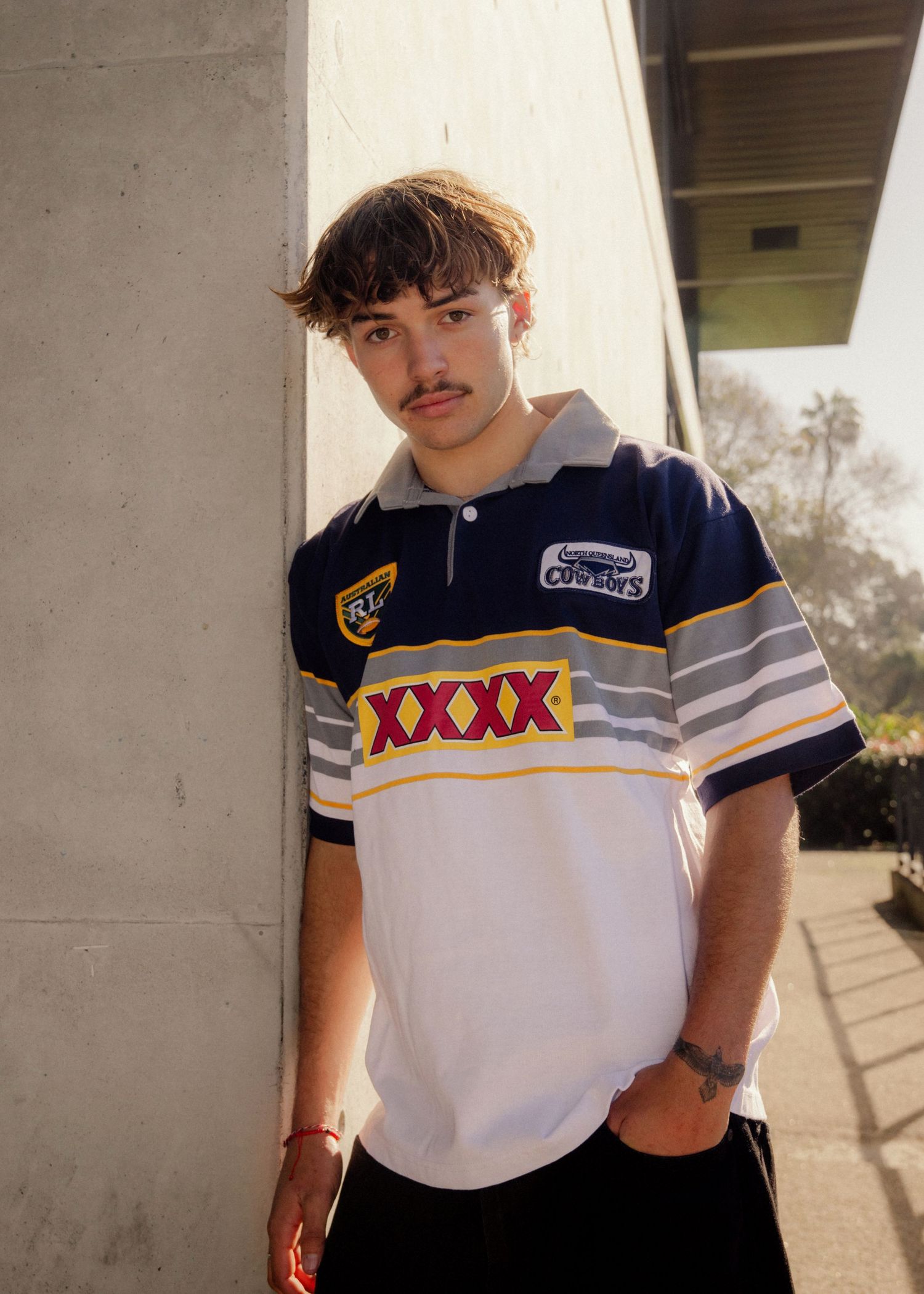 Young man in vintage XXXX North Queensland Cowboys NRL rugby jersey leaning against concrete pillar outdoors. Sutherland Shire photographer