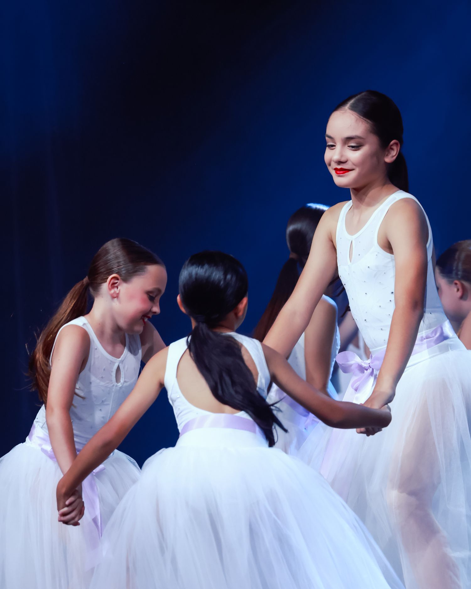 Wollongong concert photographer Ballet dancers in white dresses perform a synchronized dance routine against a dark blue backdrop.