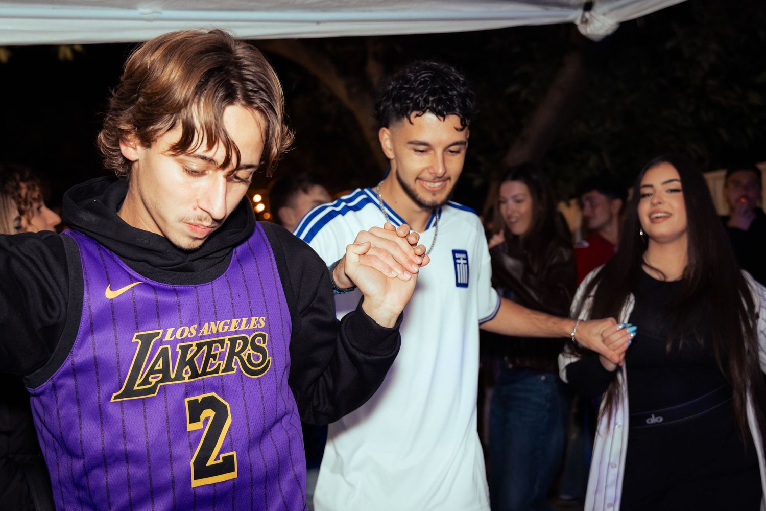 Young people dancing at a nighttime outdoor party, wearing a Lakers jersey and casual attire.