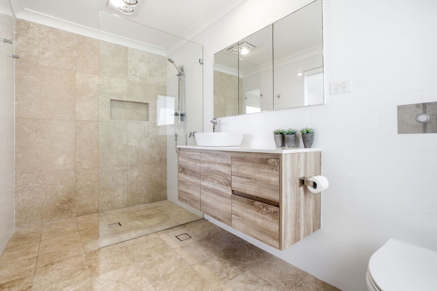 Modern bathroom with floating wood vanity, large walk-in shower, beige tiles, and triple mirror cabinet.