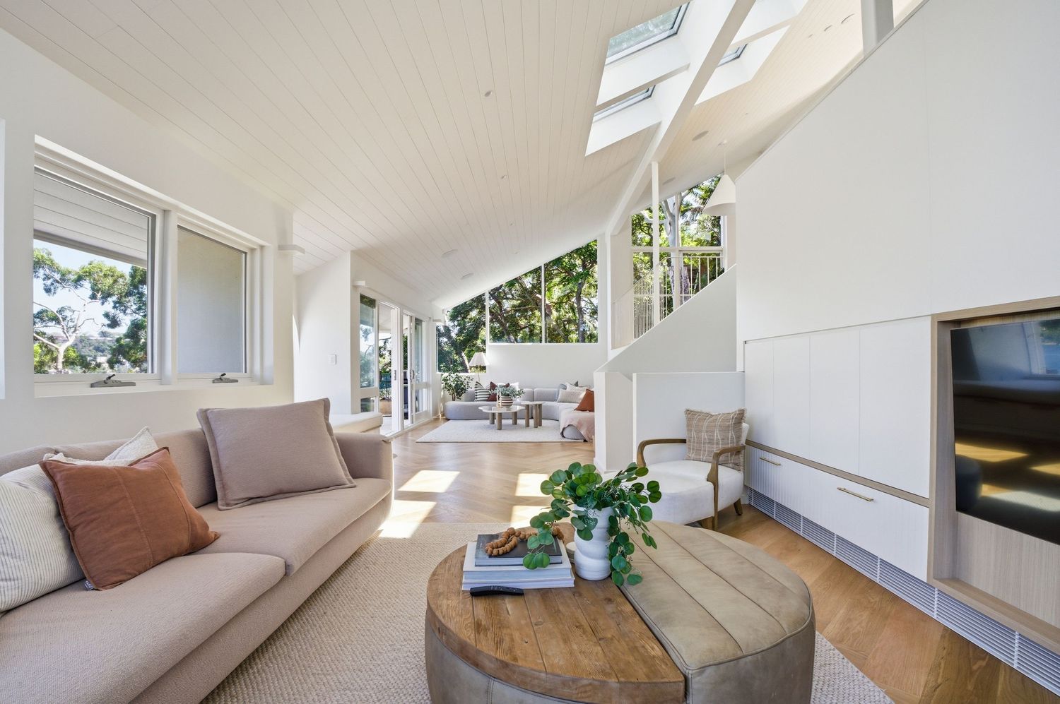 Real Estate Modern white living room with built-in bench seating, hardwood floors, and large windows letting in natural light.