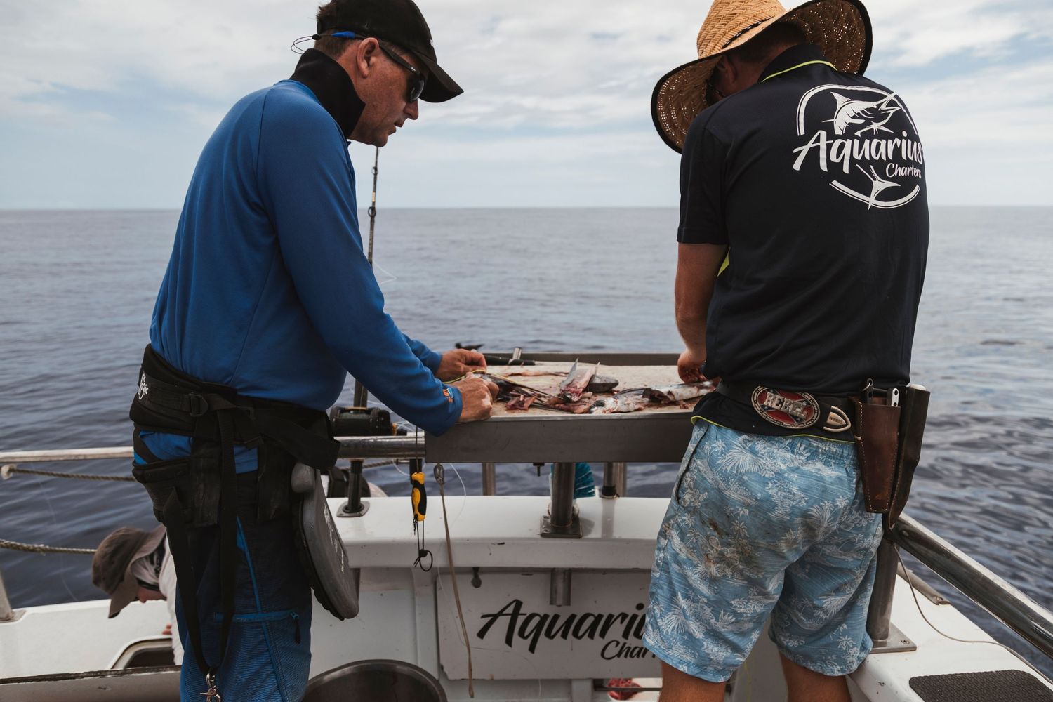 Two anglers on an Aquarius Charter boat sorting fishing gear over the ocean on a sunny day.