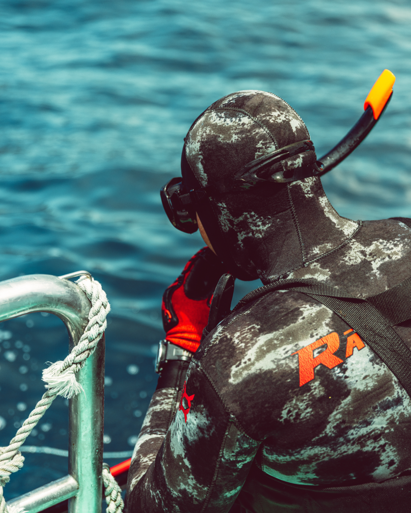 Underwater spearfishing diver in black wetsuit and snorkelling gear swimming near the surface of blue ocean water.