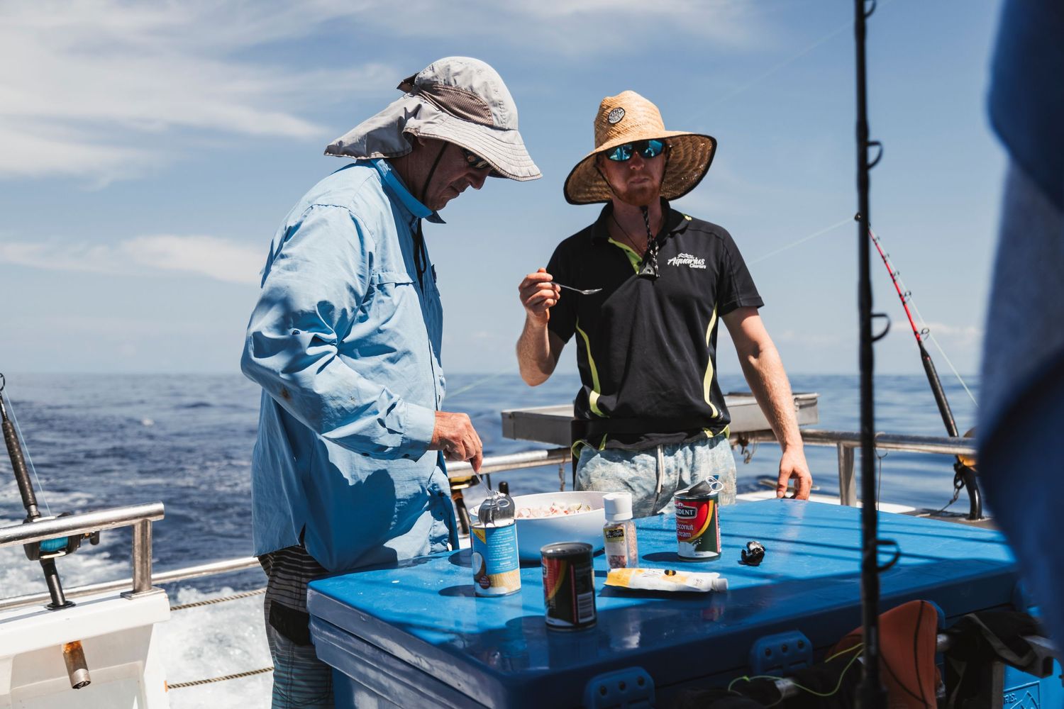 Two anglers on a fishing boat reviewing tackle and gear on a blue table with ocean views on a sunny day.