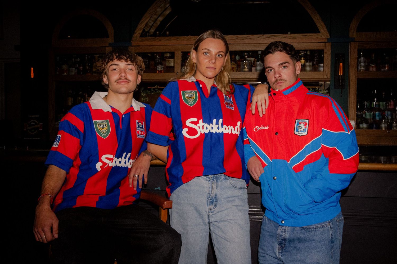 Three people wearing retro Stockland-sponsored red and blue soccer jerseys posing together at a bar. Sutherland Shire photographer