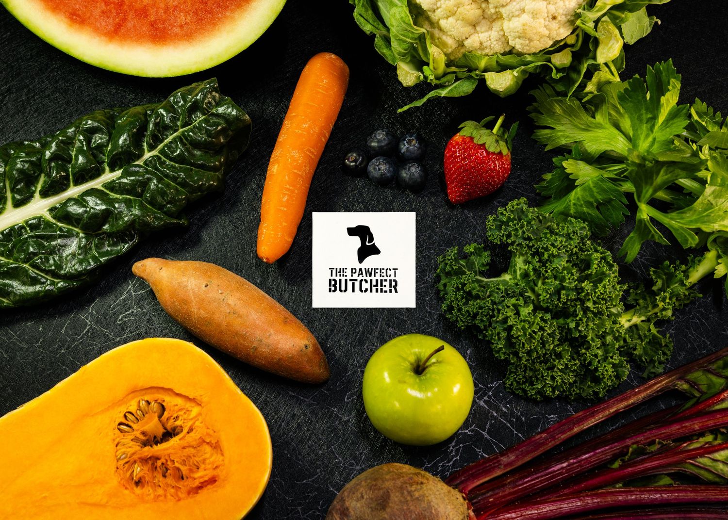 Food and product photography and videography Fresh produce including watermelon, carrots, greens and fruits arranged on dark background.