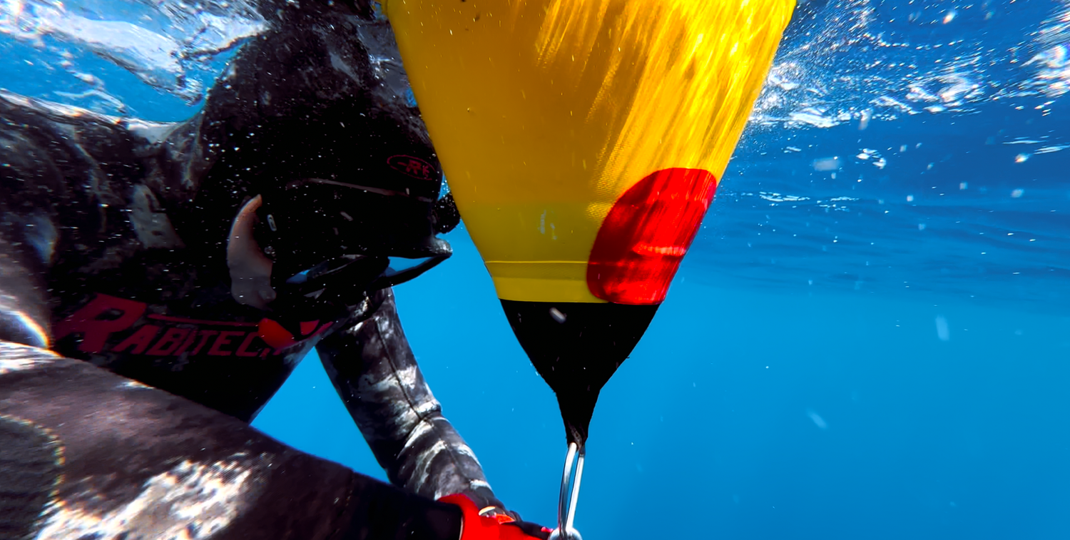 Sydney Sutherland Documentary and Film Underwater view of diving equipment with yellow and red lift bag against bright blue water.