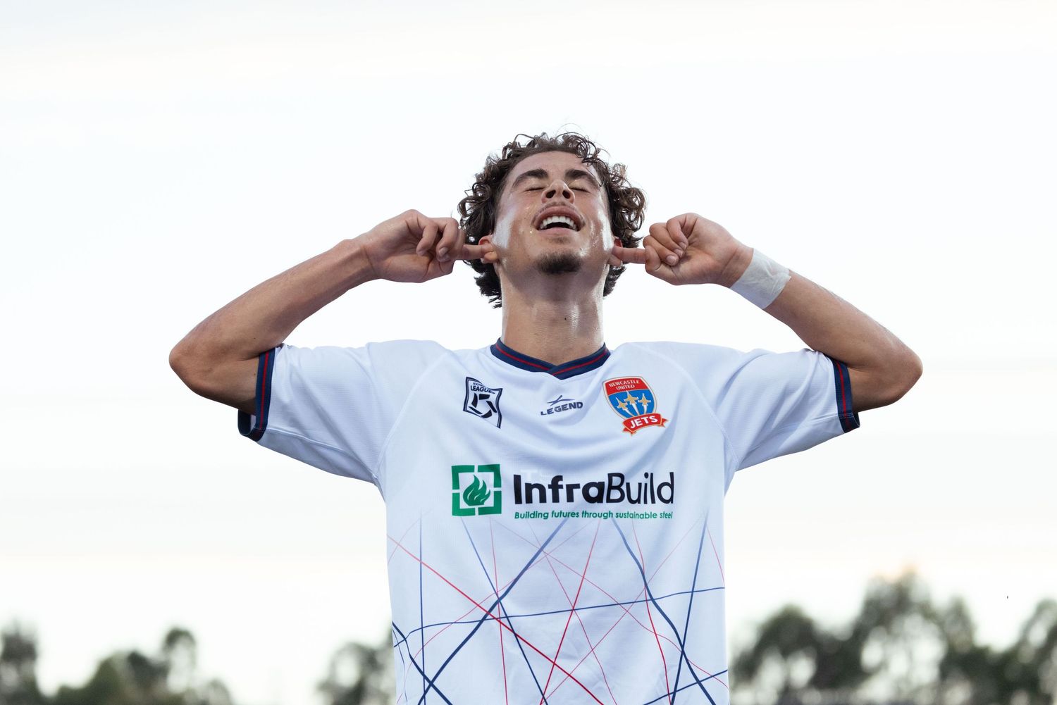 wollongong sports photographer captures Soccer player in white InfraBuild jersey celebrating with hands raised to ears.