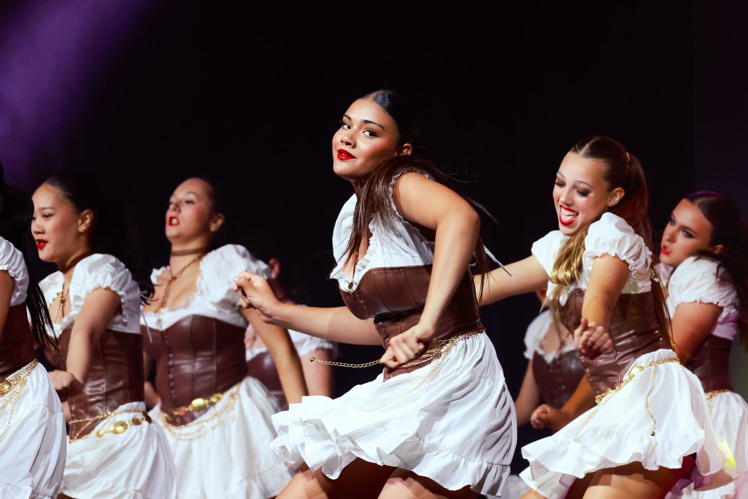 Sutherland Shire dancers, photography of dance ensemble in white dresses performing a synchronized routine on a dark stage.