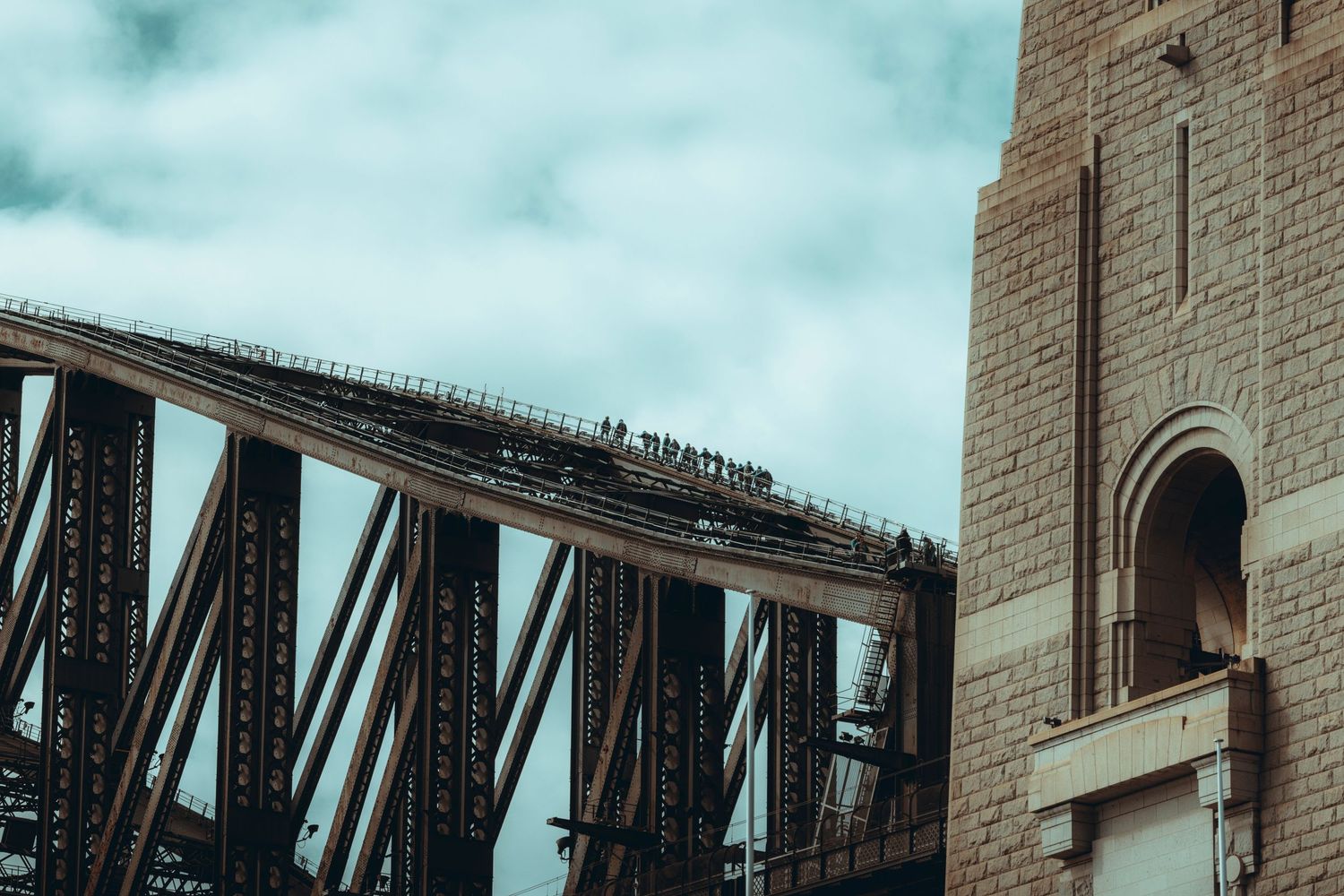 Close-up view of Sydney Harbour Bridge steel arch structure with stone pylon against cloudy sky. Sutherland Shire photographer