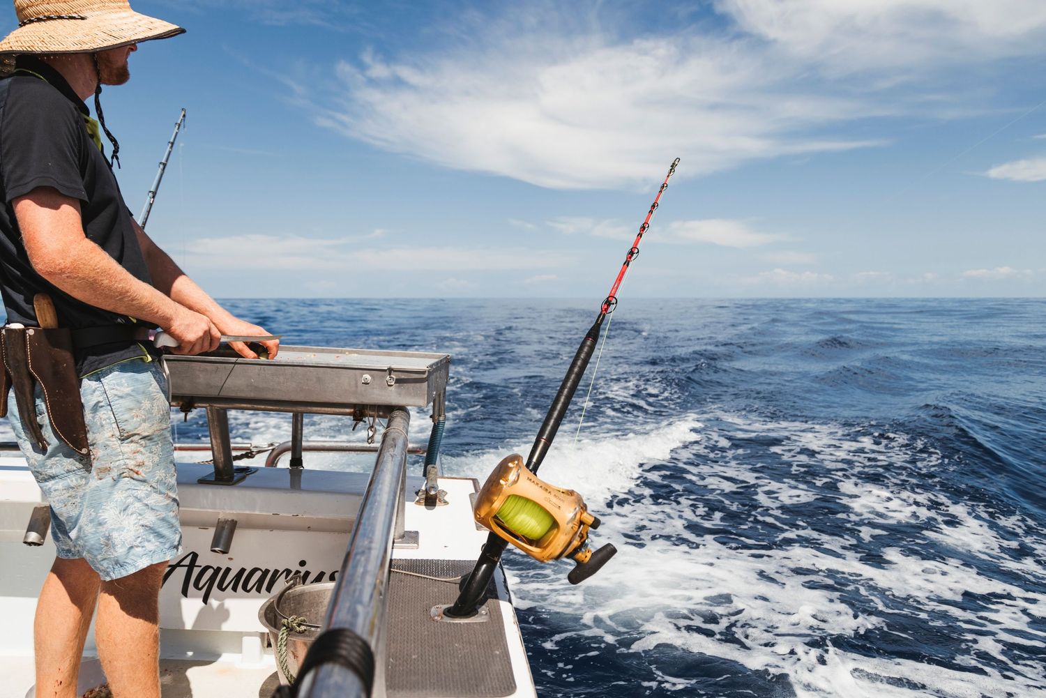 Person deep sea fishing from a boat named Aquarius on a sunny day with blue ocean waves in the background.