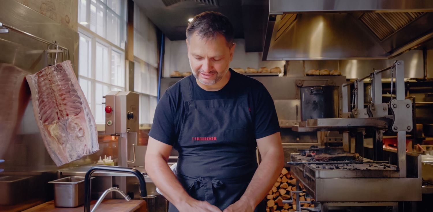 A chef in a black uniform smiles while working in a professional kitchen with equipment and ingredients. Sutherland Shire videographer