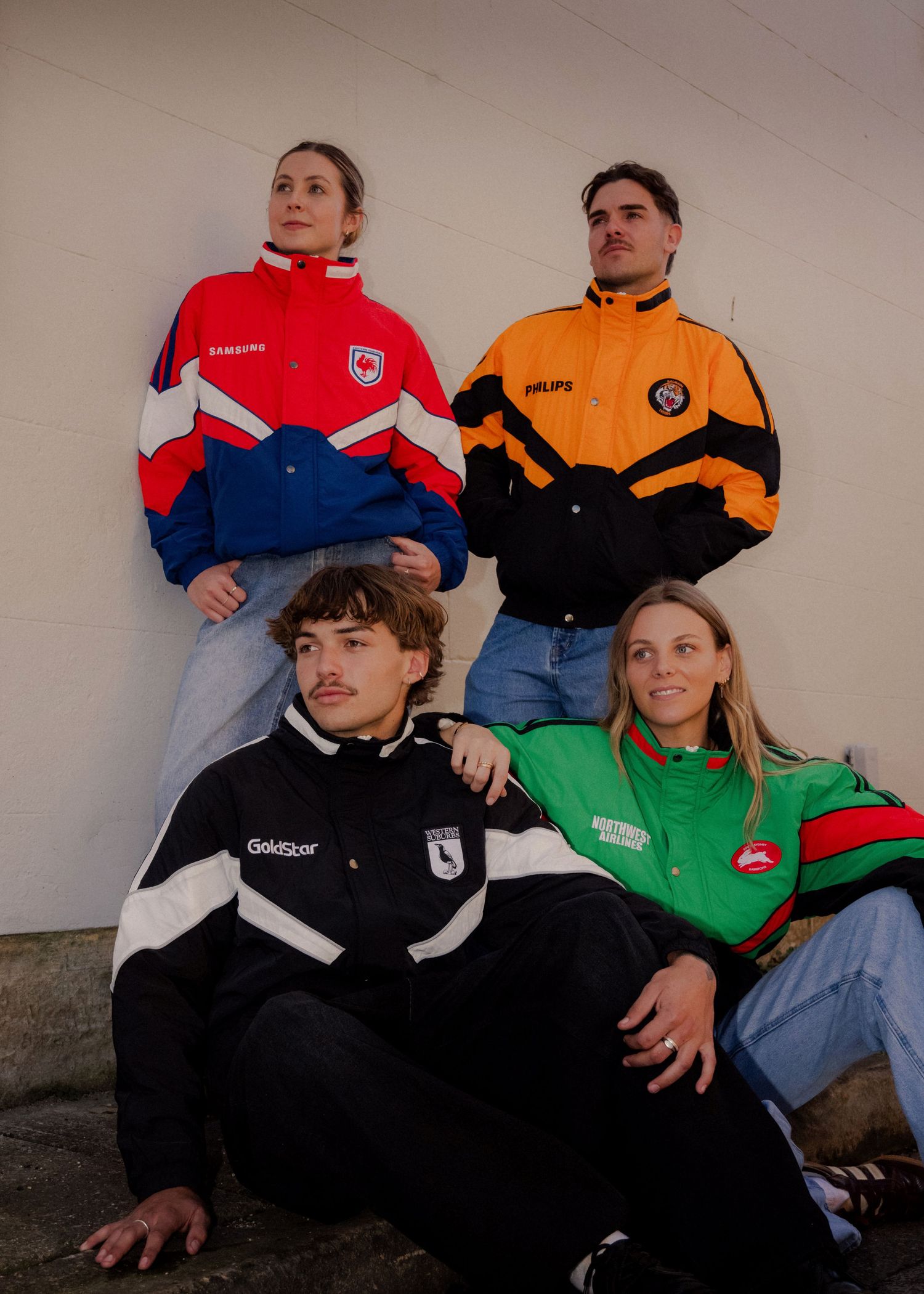 Four young people wearing vintage NRL team jackets pose together against a concrete wall. Sydney Photographer