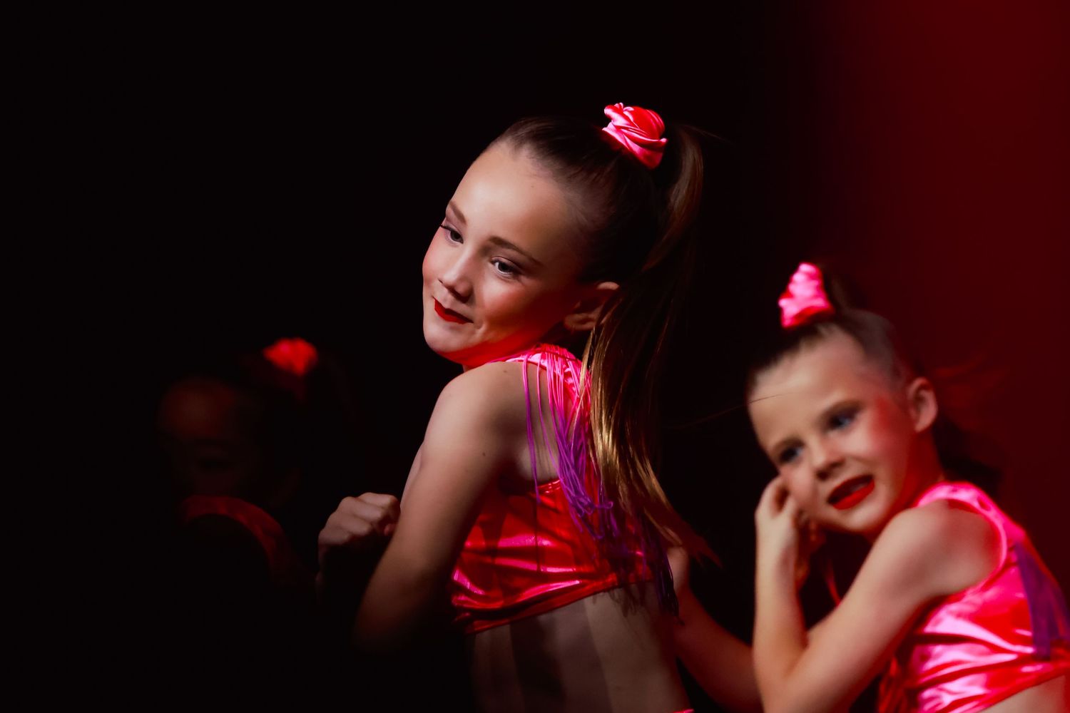 Dance concert photography of dancers in shiny red costumes perform under dramatic stage lighting performing at Sutherland Shire
