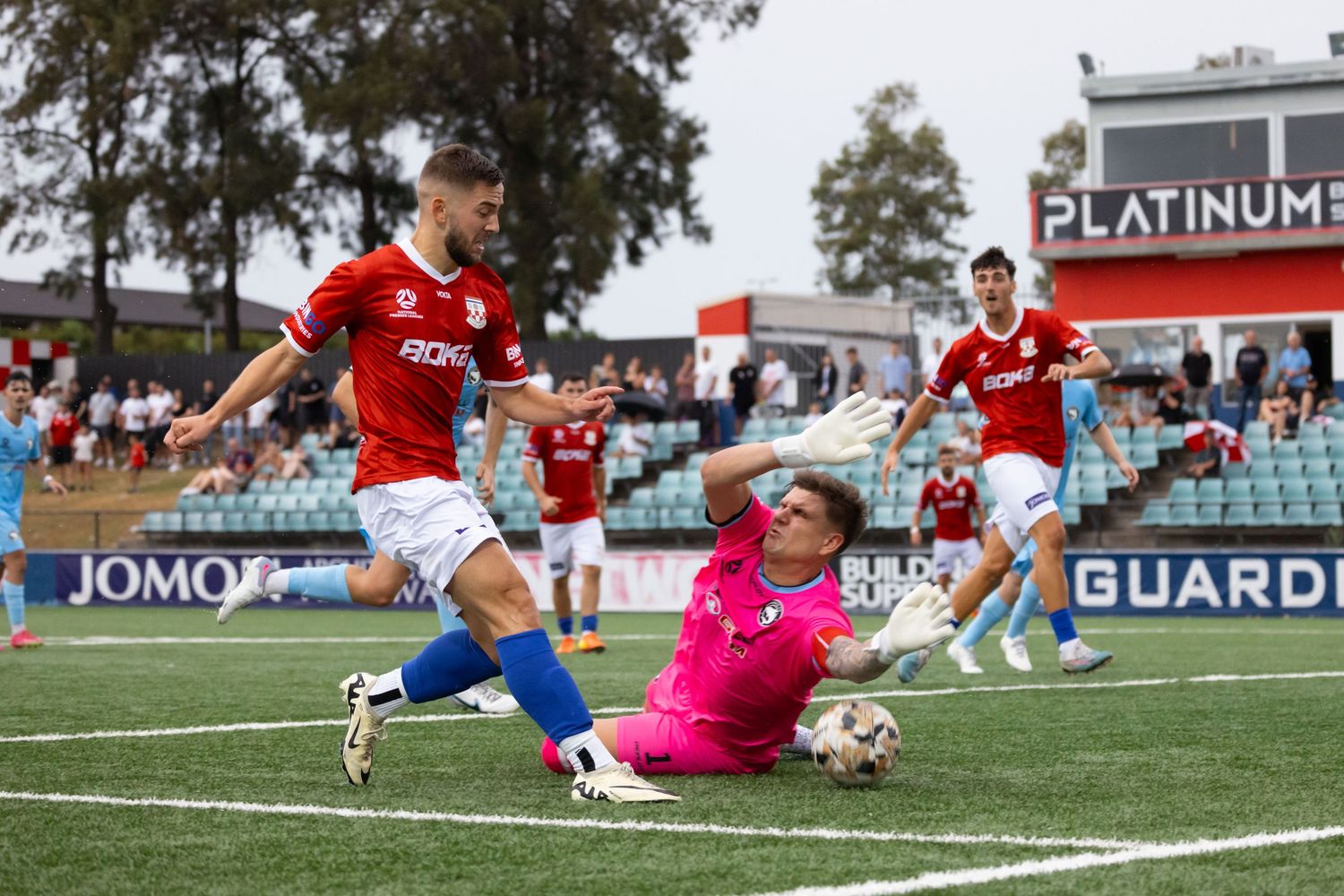 Professional football photography of Sydney United vs Sutherland players in action on a professional field with advertising boards visible.