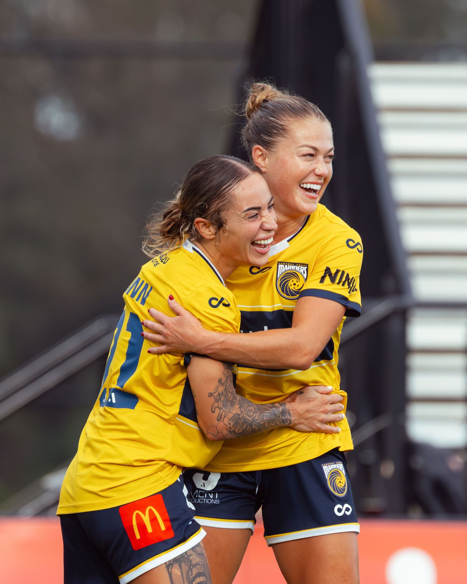 Professional football photography of central coast mariners soccer players in yellow jerseys celebrating with hugs after scoring.