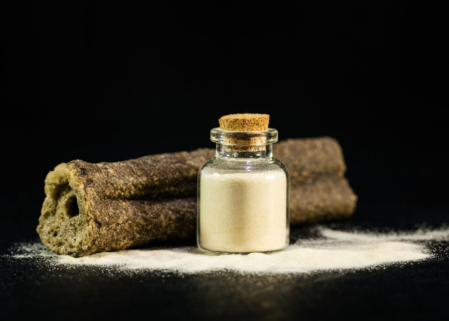 Small glass jar with cork lid filled with white powder beside two cinnamon sticks on dark background.