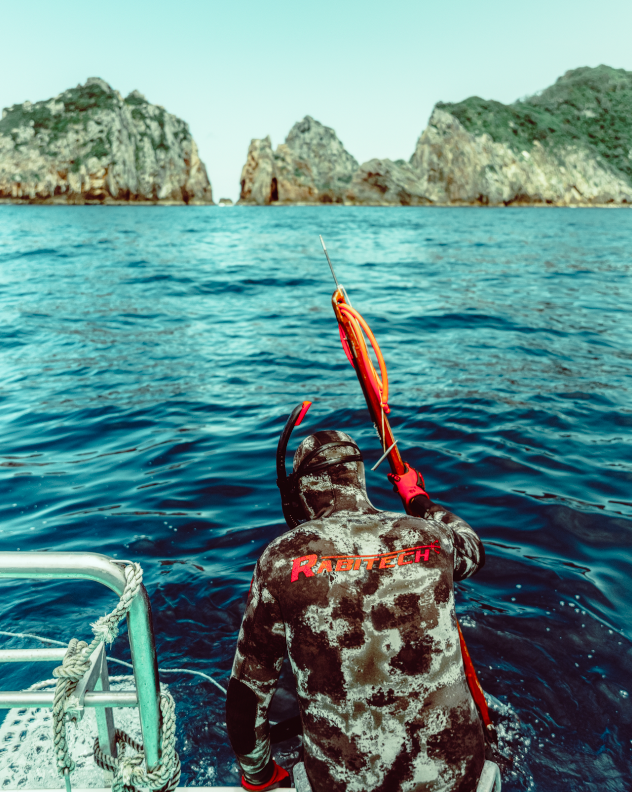 Spearfishing diver with snorkel uderwater gear swimming in crystal clear blue waters near rocky coastal cliffs in Wollogong Illawarra