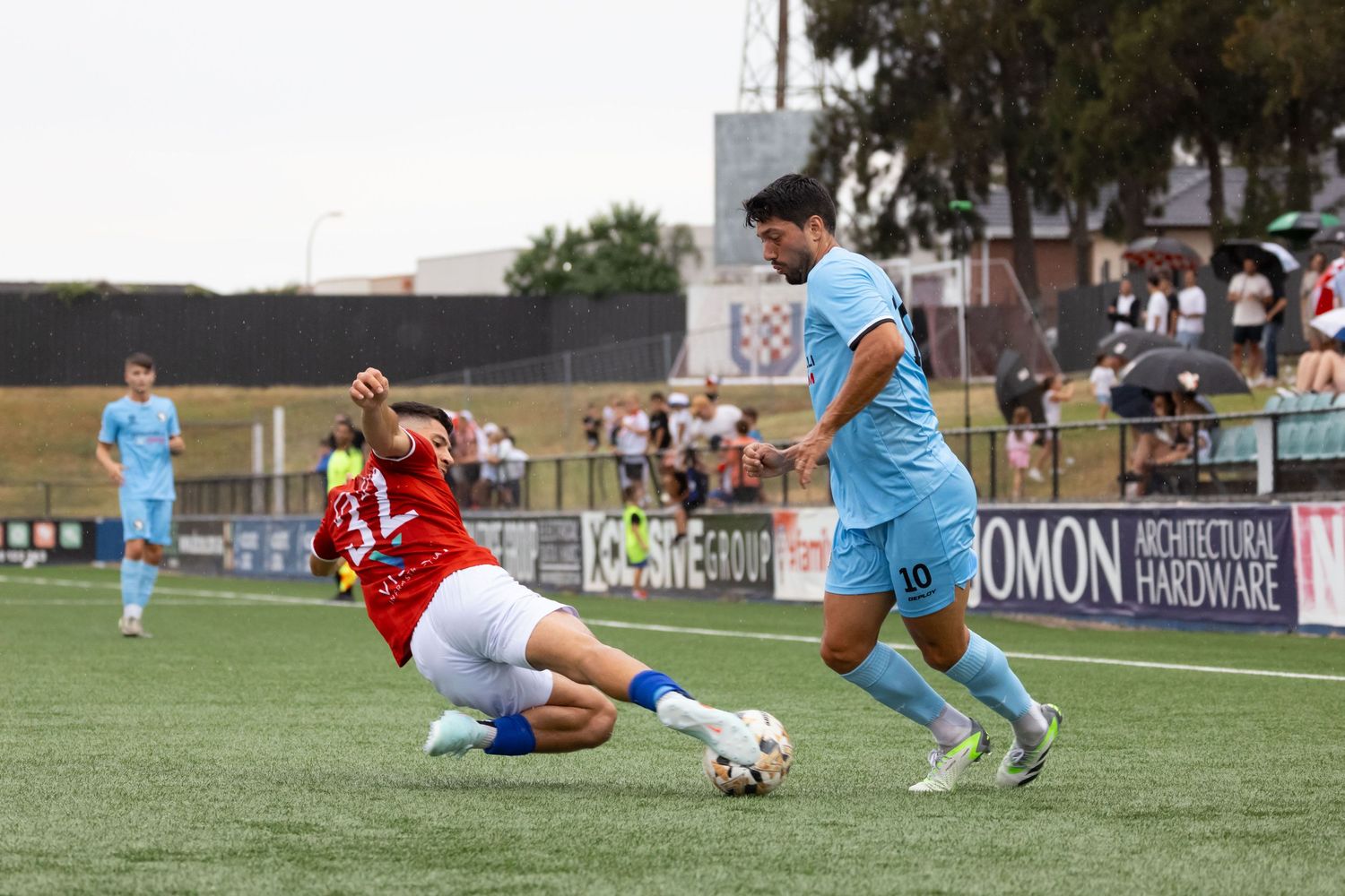 Wollongong photographer Intense soccer tackle between players in red and light blue uniforms during match play.