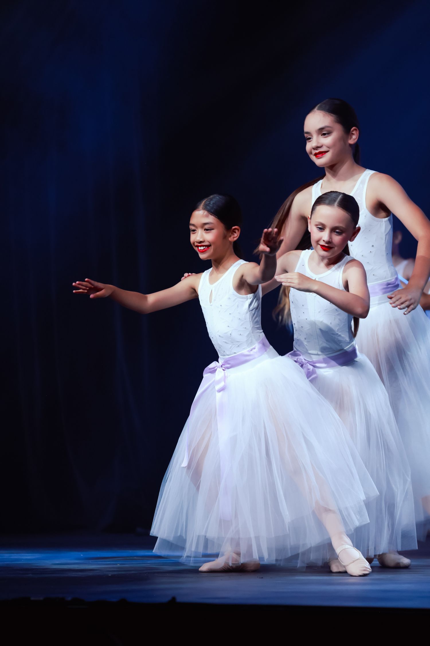 Wollongong concert photographer Young dancers in flowing white tutus perform gracefully on stage with blue backdrop.