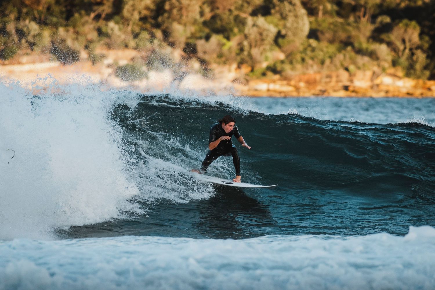 Wollongong photographer captures Surfer rides large wave against dramatic coastal cliff backdrop.