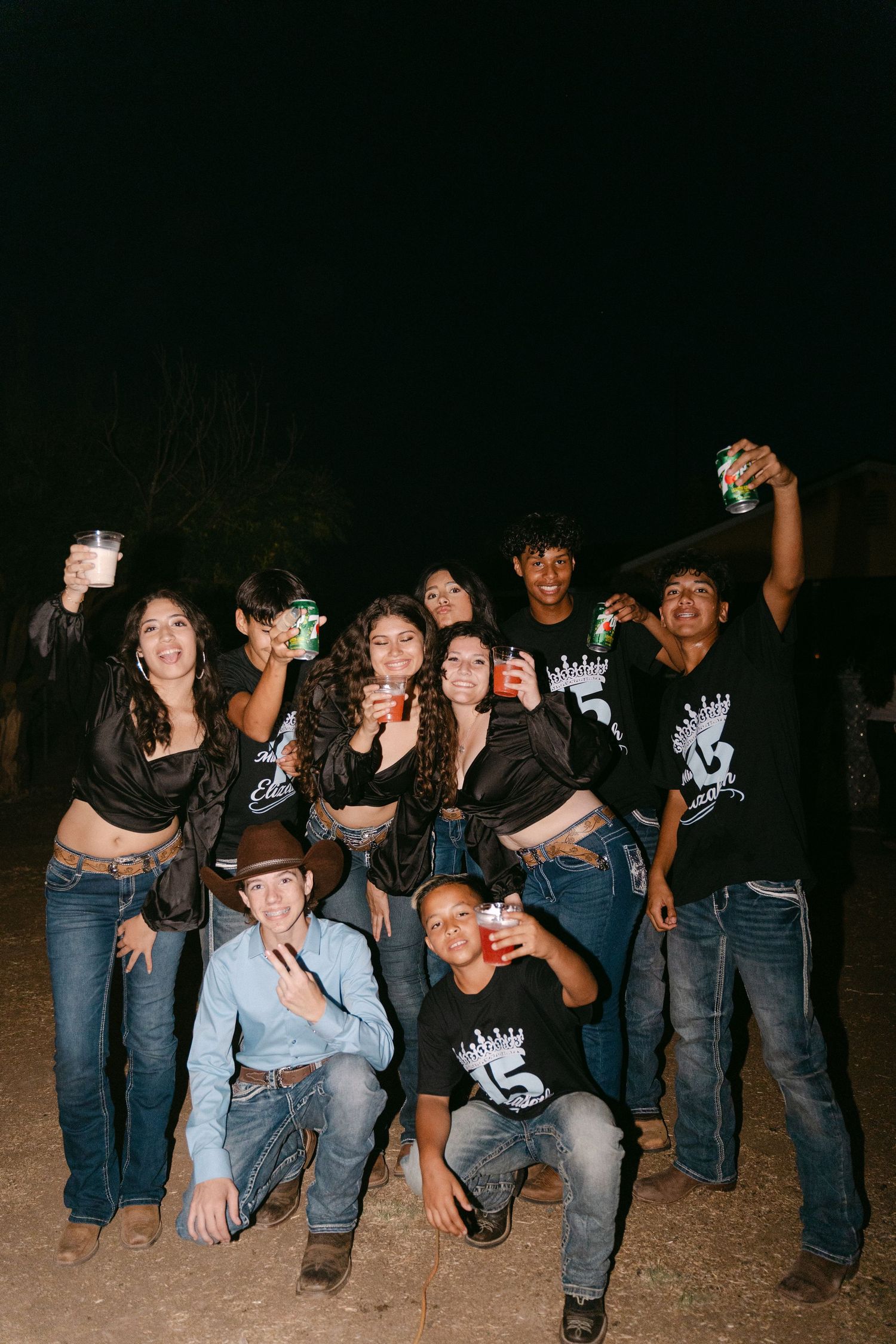 Group wearing matching black t-shirts poses together at night during celebration.