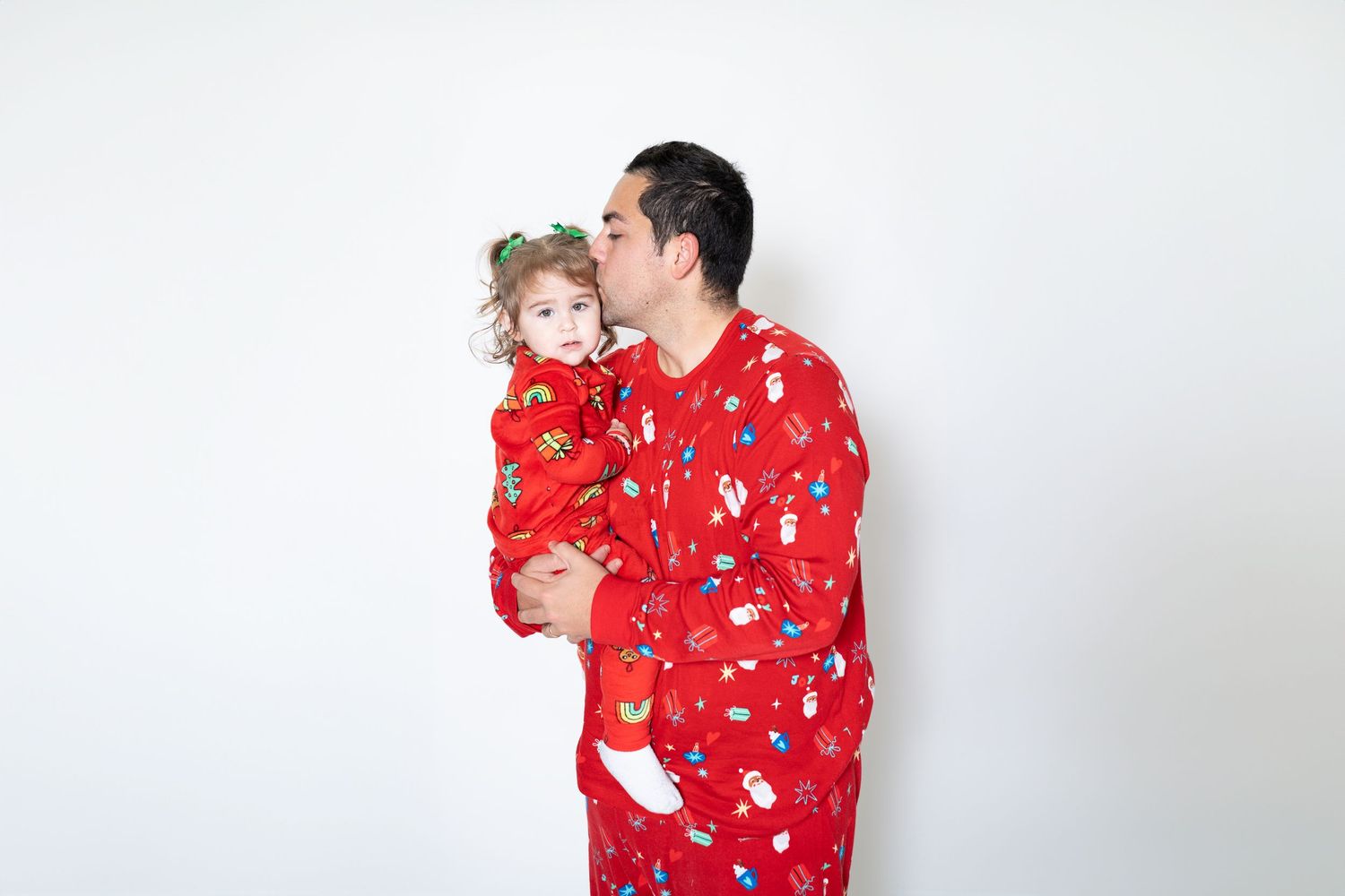 Parent and child in matching red holiday pajamas share tender moment in studio setting
