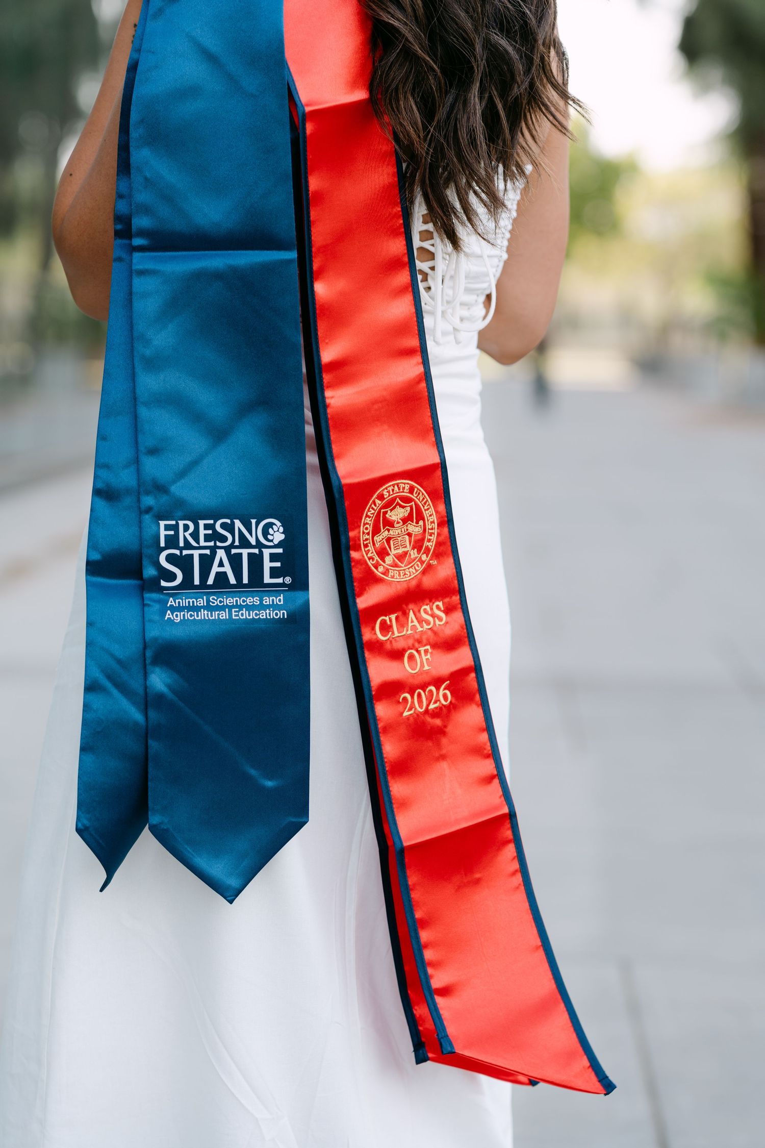 Fresno State Class of 2026 graduation stoles in blue and red worn by a student in a white dress.