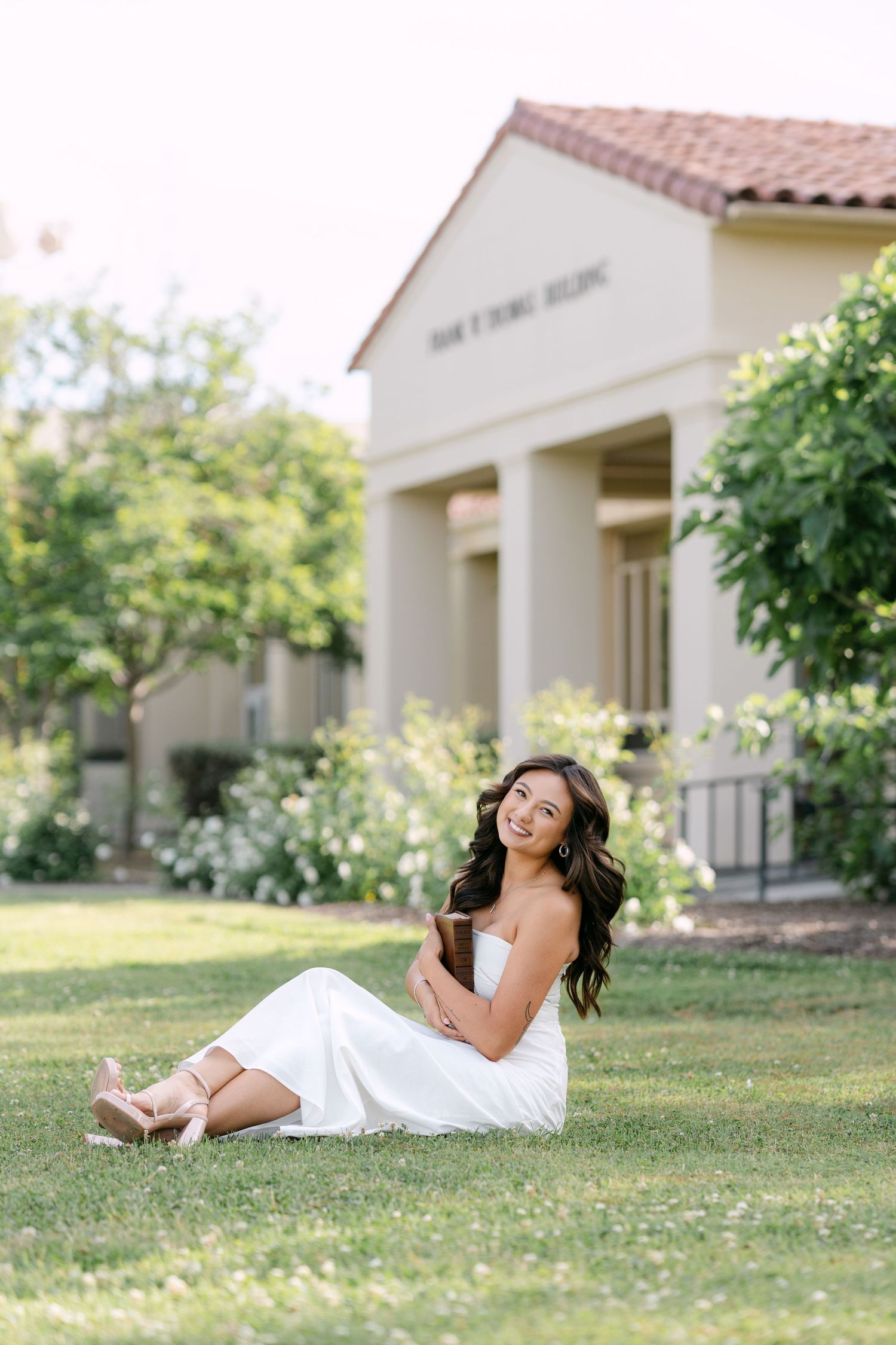 Young woman in white dress sitting on grass in front of elegant building.