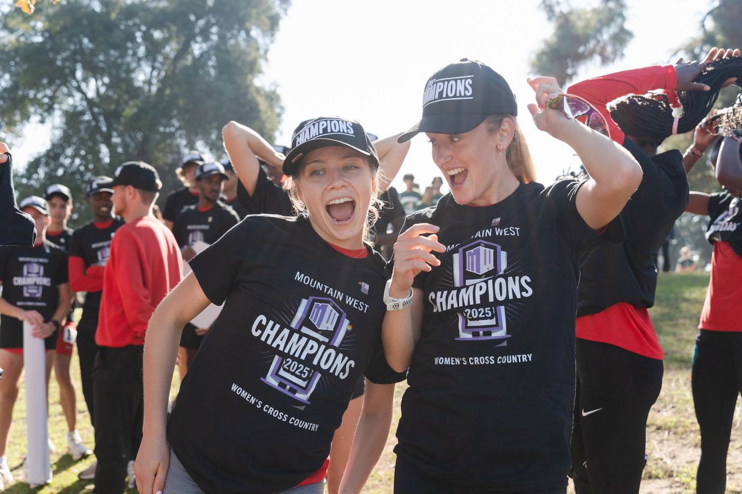 Two young fans in black championship t-shirts cheer enthusiastically at an outdoor sporting event.